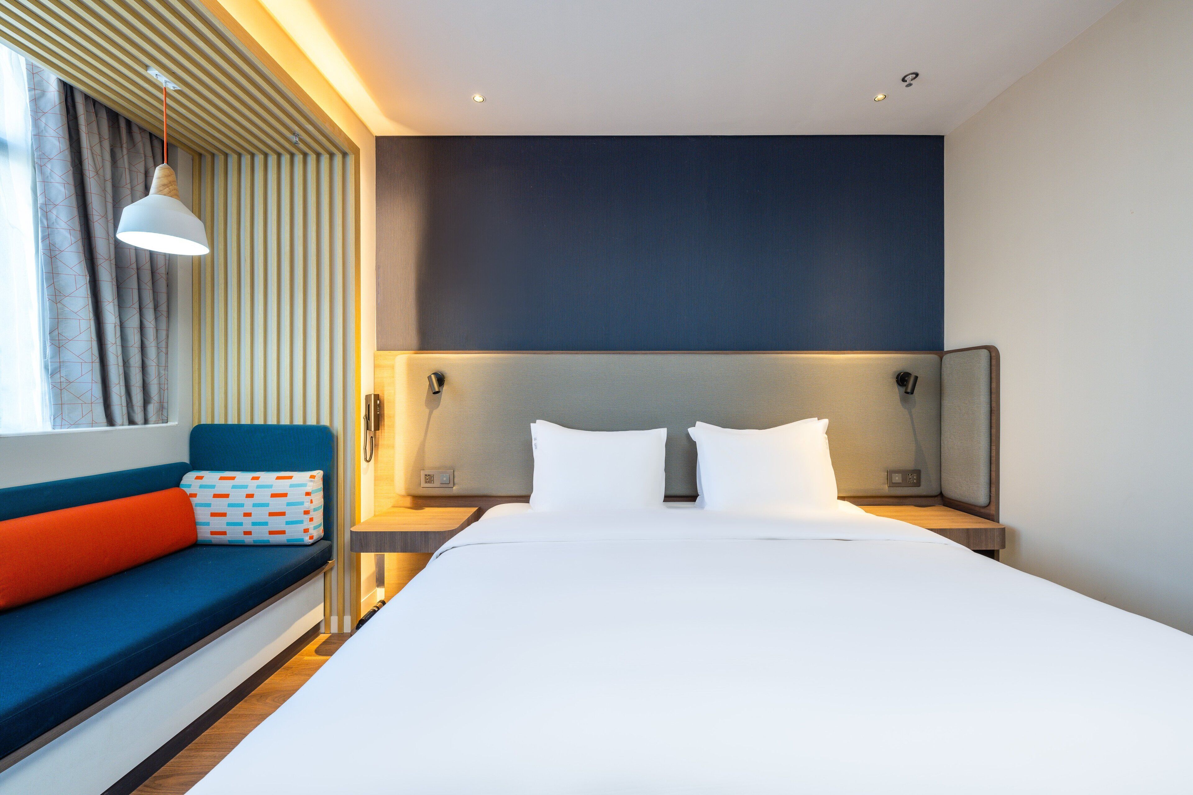 Een moderne hotelkamer met een groot bed, een blauwe bank met oranje kussens en een wandmontage hoofdbord.