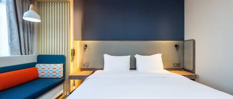 Een moderne hotelkamer met een groot bed, een blauwe bank met oranje kussens en een wandmontage hoofdbord.