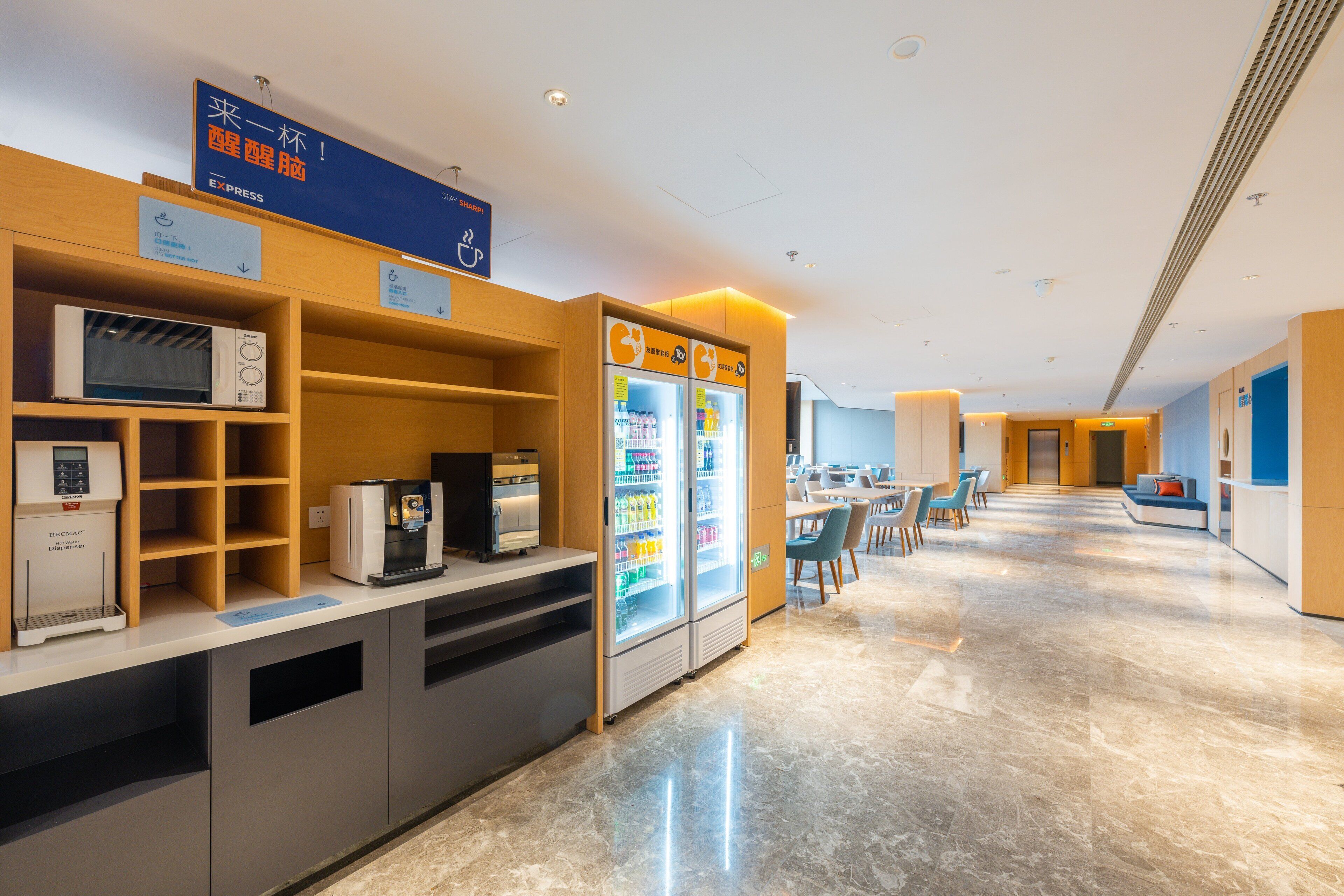 Un moderno hall de hotel con una máquina de café, un microondas y dos refrigeradores.