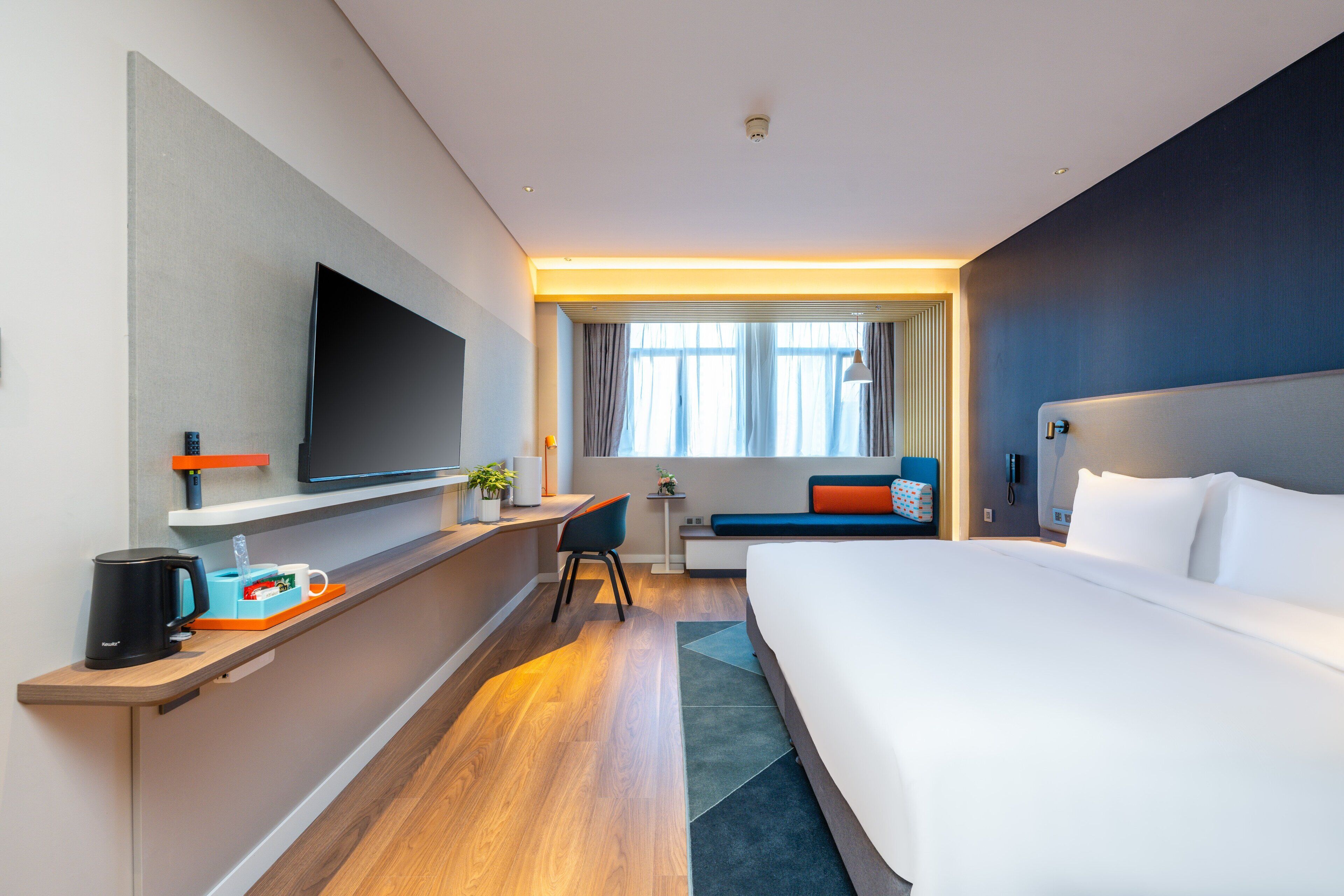 Une chambre d’hôtel moderne dotée d’un grand lit, d’une télévision à écran plat, d’un bureau avec une machine à café et d’une fenêtre avec des rideaux.