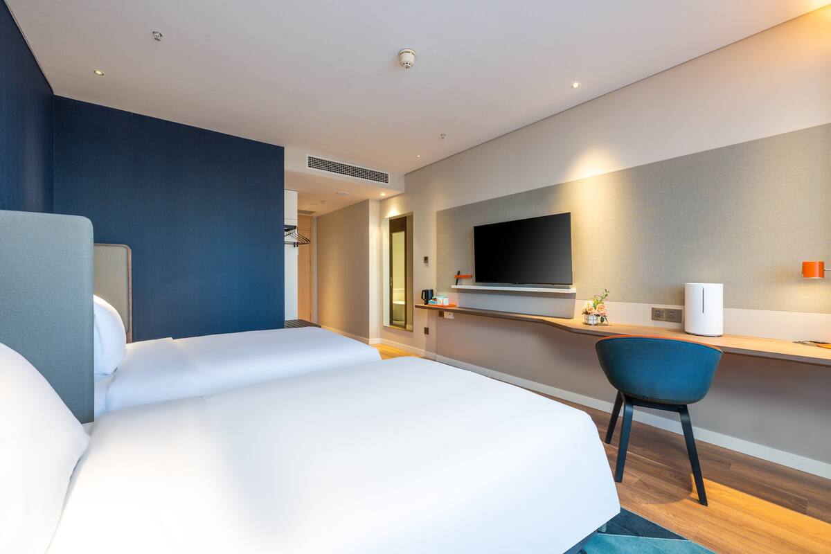 A modern hotel room with a large bed, a desk with a flat-screen TV, and a chair.