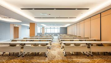 A conference room with rows of tables and chairs, a patterned carpet, and a view of the city through large windows.
