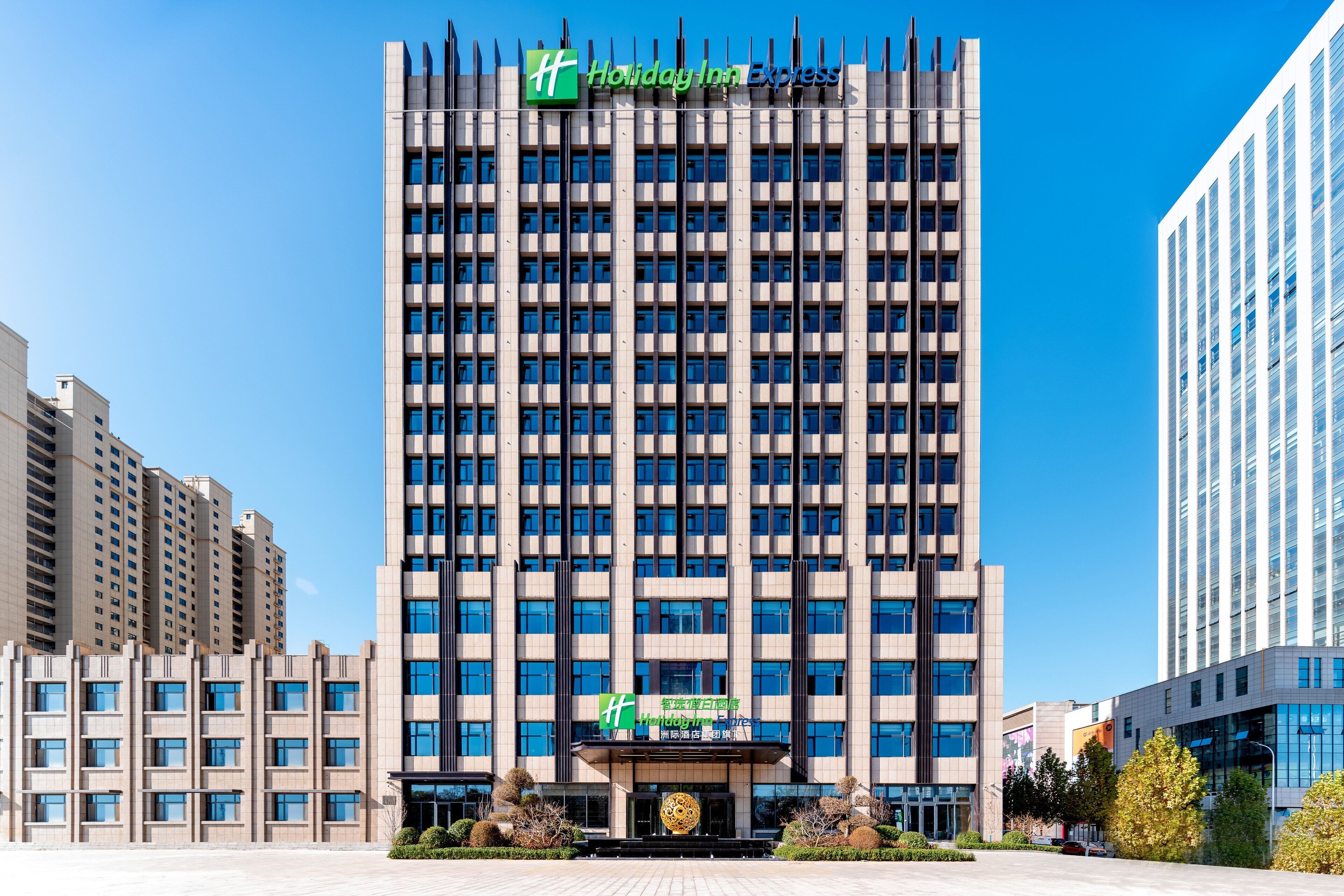 Un edificio alto de hotel con el letrero Holiday Inn Express, varios pisos y una entrada central con un logotipo grande.