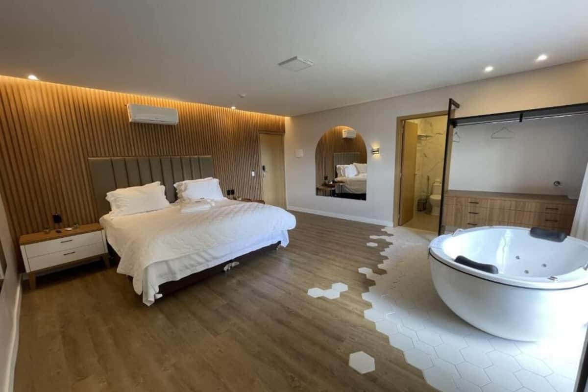 Una habitación de hotel moderna con una cama grande, un vestidor y un baño separado con hidromasaje.