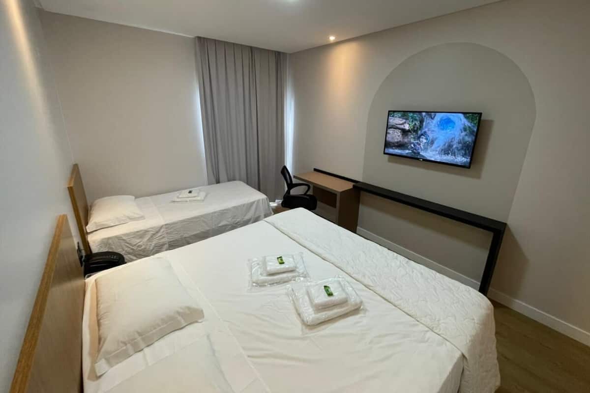 Habitación de hotel con dos camas, un televisor montado en la pared y un escritorio con una silla.