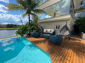 Een modern zwembadgedeelte met een houten terras, blauwe buitenmeubels en een bord met de tekst 'Hotel do Lago'.