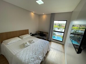 Ein Hotelzimmer mit einem großen Bett, einem Schreibtisch, einem Sessel, einem Fernseher und einem Fenster mit Blick auf einen Pool.