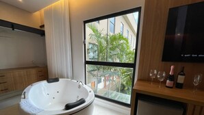 Een moderne badkamer met een ruime badkuip, een douchecabine met glazen wanden en uitzicht op een gebouw en groen.