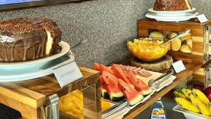Een buffet met diverse gerechten, een taart en een groot scherm waarop een strand te zien is.