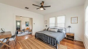 Ein Schlafzimmer mit einem Bett, einem Schreibtisch, einem Sessel, einem Deckenventilator und einem Fenster.