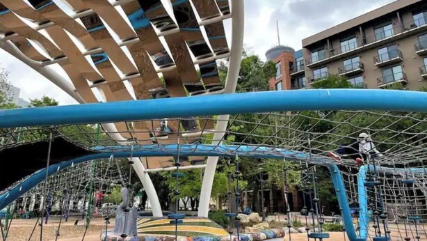 Ein Spielplatz mit Klettergerüsten und einem großen, modernen Gebäude im Hintergrund.