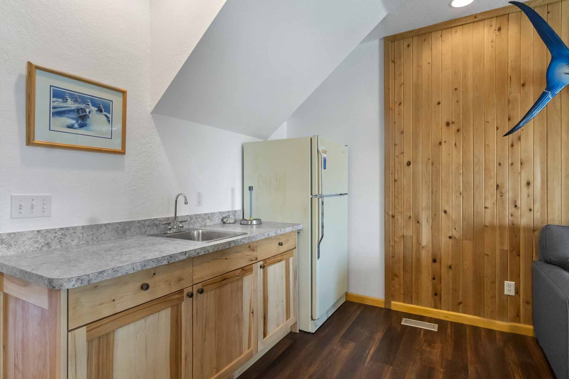 Une cuisine dotée d’un plan de travail en granit, d’un évier, de meubles en bois, d’un réfrigérateur blanc et d’un panneau mural en bois.