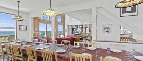 A dining area with a large table set for six, wooden chairs, and hanging lamps.