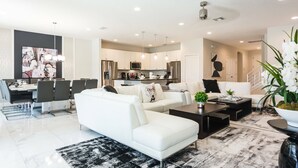 A modern living room with a white sofa, black coffee table, and a black and white rug. A kitchen with white cabinets and stainless steel appliances is visible in the background. - Relax in Style: Elegant Vacation Home in Orlando (Kissimmee)