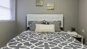 Un dormitorio ordenado con una cama grande, una mesita de noche y dos cuadros colgados en la pared.