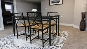 Un comedor con una mesa y sillas de metal negro, un tapete blanco y negro estampado y un cuadro en la pared.