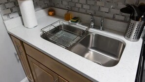 Una cocina con un lavamanos doble, un escurreplatos, un rollo de toallas de papel, un dispensador de jabón y un organizador de utensilios.