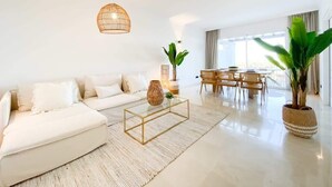 A modern living room with a white sofa, a glass coffee table, and a hanging light fixture. - Altos La Quinta | Sea View Luxury Penthouse (Benahavís)