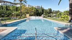 A swimming pool with clear blue water, surrounded by palm trees and a well-maintained lawn. - Altos La Quinta | Sea View Luxury Penthouse (Benahavís)