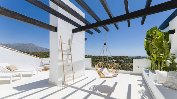 A rooftop terrace with white furniture, a hanging chair, and a view of the landscape. - Altos La Quinta | Sea View Luxury Penthouse (Benahavís)