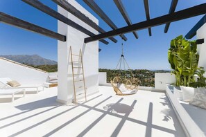 Una terraza en la azotea con mobiliario blanco, una silla colgante y vistas al paisaje.