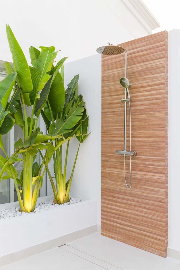 Un baño moderno con cabina de ducha de madera, bañera blanca y exuberantes plantas verdes.