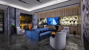 Eine moderne Lobby mit einem blauen Sofa, weißen Ohrensesseln, einem Couchtisch und einem Fernseher an der Wand.