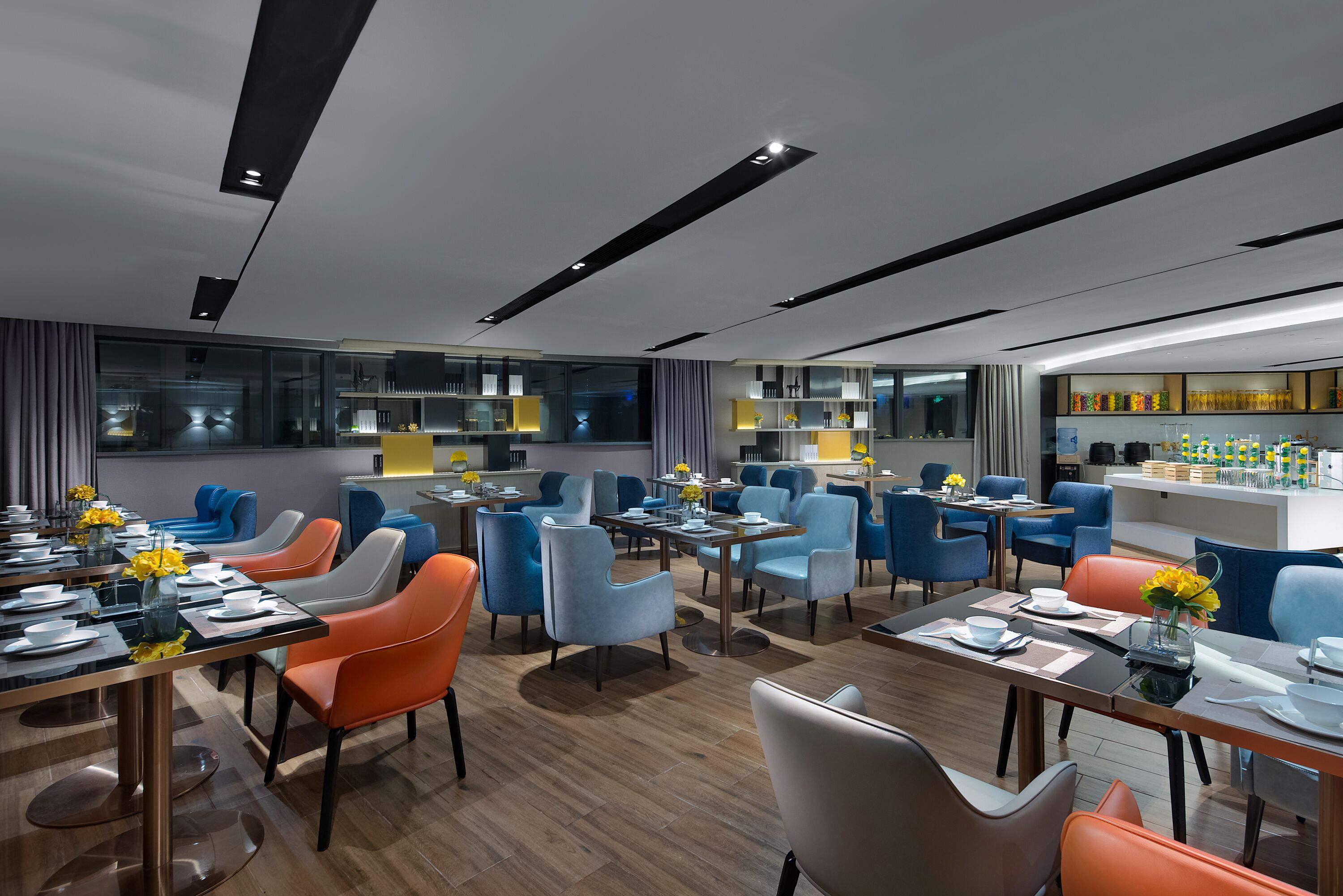 A modern dining area with multiple tables and chairs, a kitchen area, and a bar.