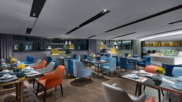A modern dining area with multiple tables and chairs, a kitchen area, and a bar.