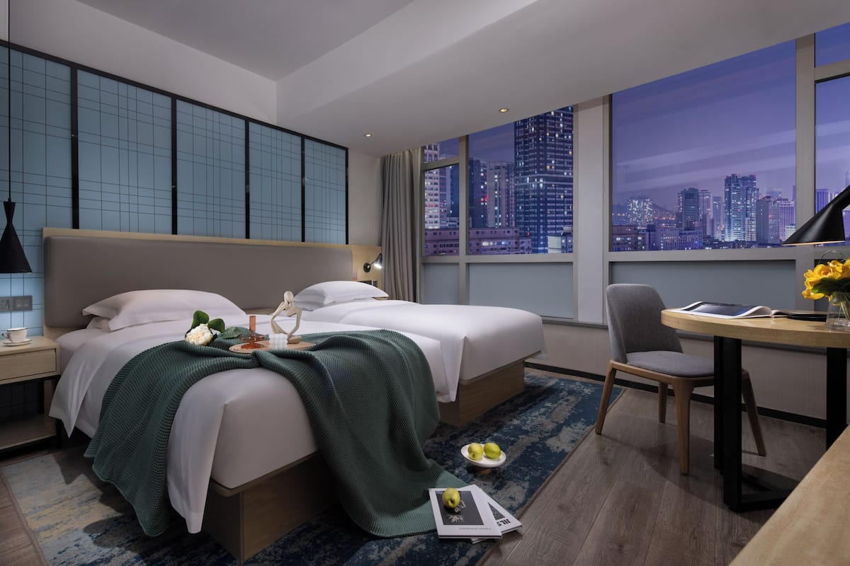 Una habitación de hotel moderna con una cama grande, un escritorio y vistas a un paisaje urbano nocturno.