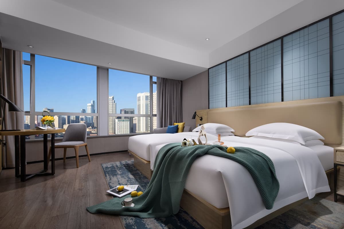 Una habitación de hotel moderna con dos camas, un escritorio y un ventanal amplio con vistas a la ciudad.