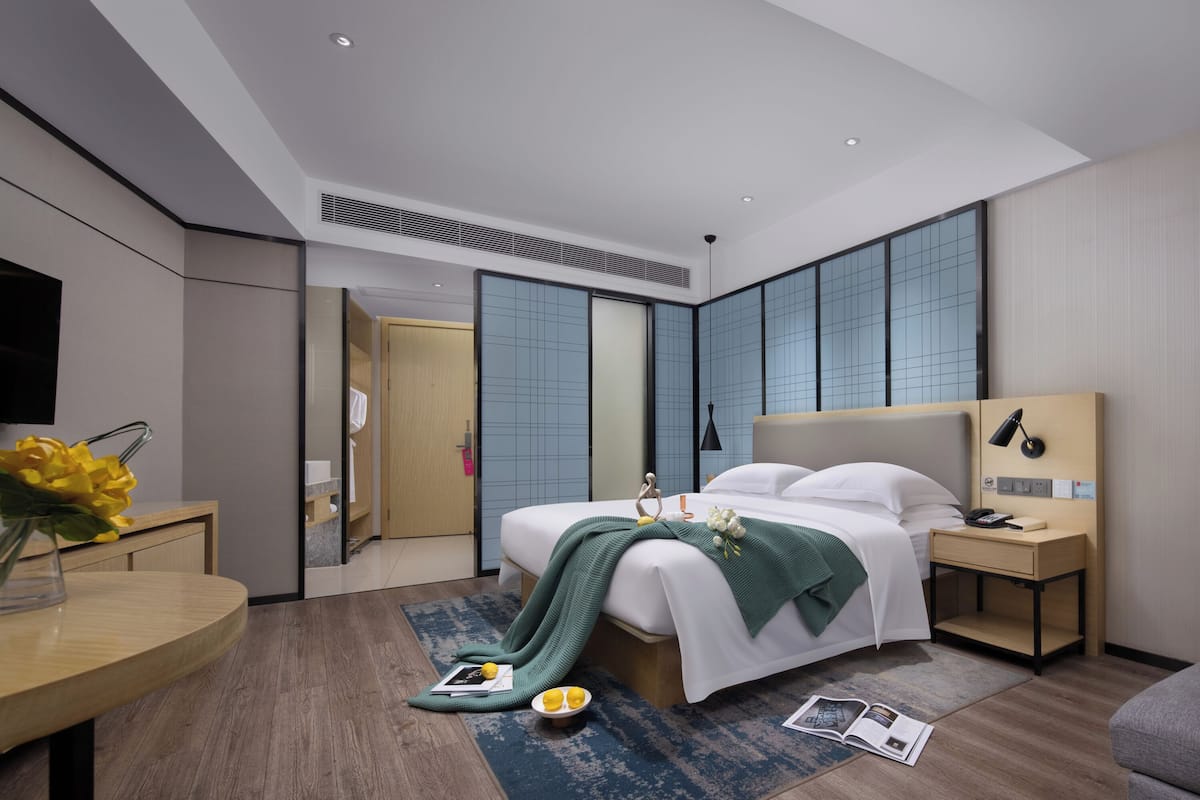 Una habitación de hotel moderna con una cama grande, mesitas de noche, un escritorio y un espejo.