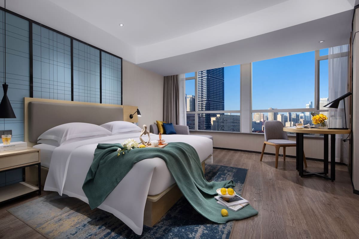 Una habitación de hotel moderna con una cama grande, un escritorio y vistas del horizonte de la ciudad.