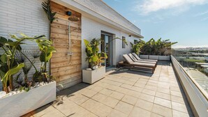 A modern rooftop terrace with a white brick wall, wooden accents, and potted plants.