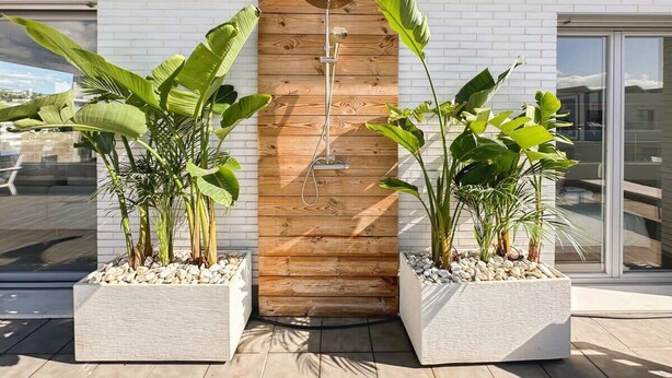 A modern building with a wooden door, potted plants, and a metal shower head.