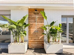 Un edificio moderno con una porta in legno, piante in vaso e un soffione doccia in metallo.