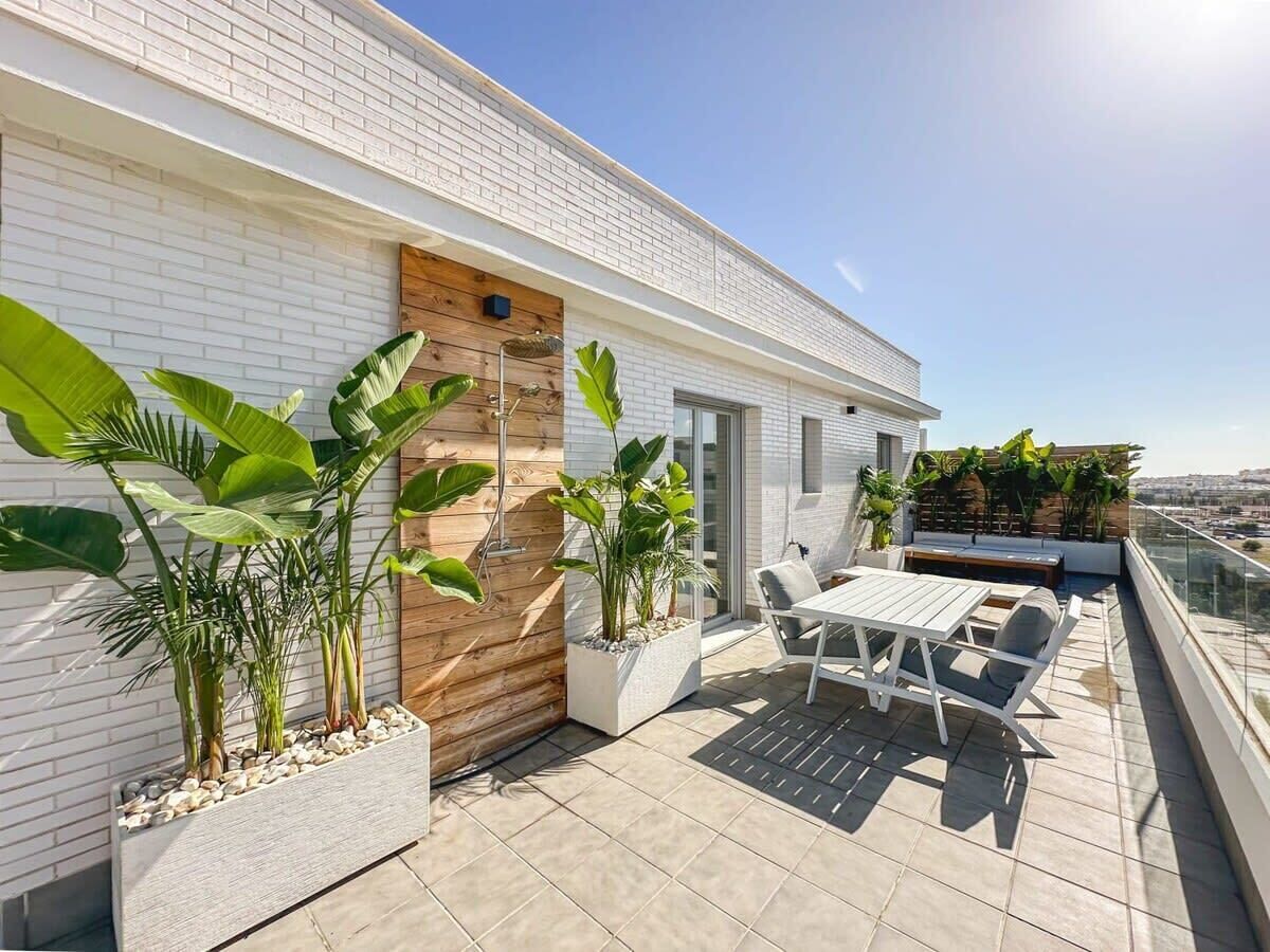 Une terrasse moderne sur le toit, avec un mur en briques blanches, une porte en bois et un espace détente comprenant une table et des chaises.