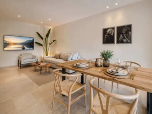 A modern living room with a sofa, a dining table set for four, and a large painting on the wall.