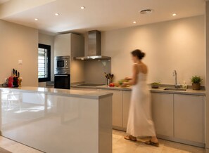 A modern kitchen with a central island, stainless steel appliances, and a woman preparing food.