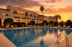 Une piscine avec des chaises longues et un grand bâtiment doté de balcons et d’un palmier.