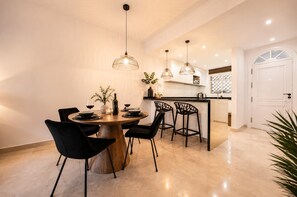 Ein Essbereich mit einem runden Holztisch, schwarzen Stühlen, Pendelleuchten und einer Küche im Hintergrund.