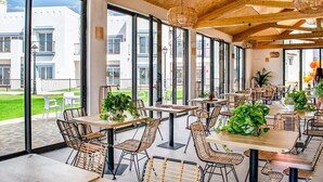 A spacious indoor dining area with large windows, wicker furniture, and potted plants.