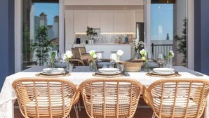 An outdoor dining area with a table set for four, surrounded by wicker chairs, and a kitchen visible through an open door.