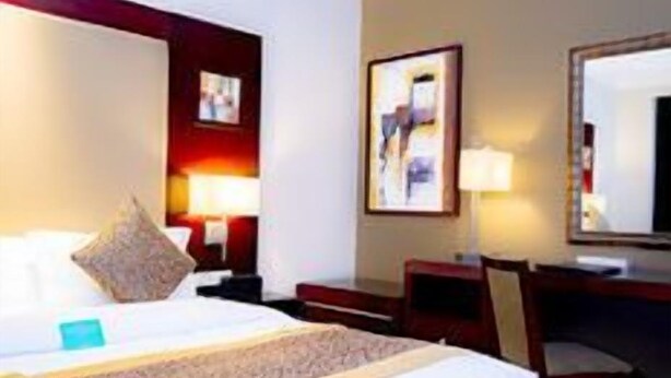 Une chambre d’hôtel comprenant un lit, une table de chevet, une lampe, une chaise et un grand miroir.
