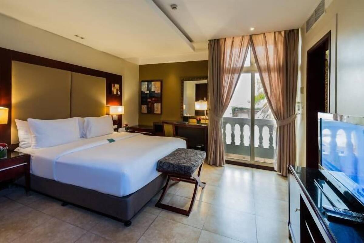 Une chambre d’hôtel avec un grand lit, des lampes de chevet, une télévision, un bureau et un balcon avec des rideaux.
