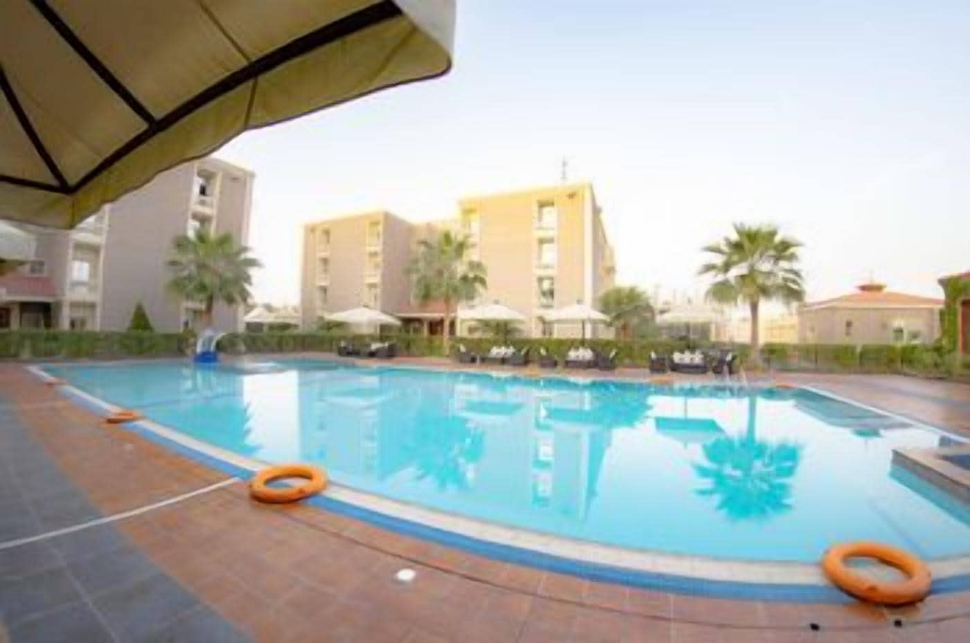 A swimming pool with a tiled deck, surrounded by palm trees and buildings.