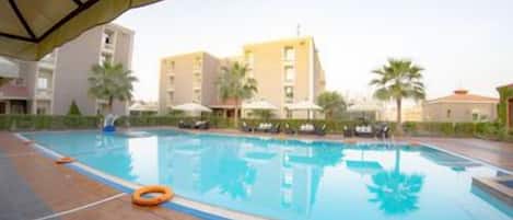 A swimming pool with a tiled deck, surrounded by palm trees and buildings.