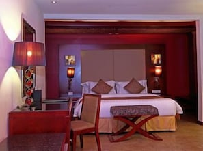 Quarto de hotel com uma cama, abajures, uma cadeira e uma mesa.