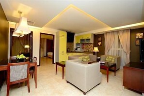 Une chambre d’hôtel avec un coin repas, un canapé, une télévision et une cuisine en arrière-plan.
