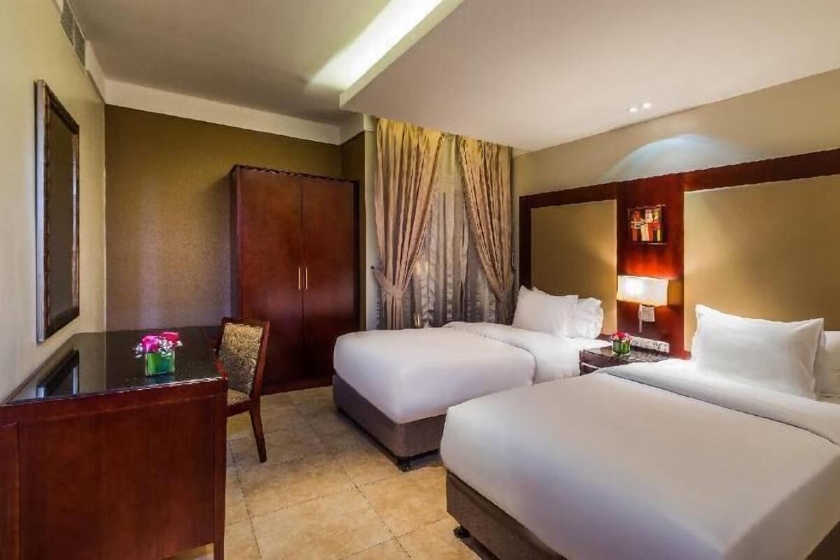 Une chambre d’hôtel avec deux lits, un bureau, une chaise et une armoire.